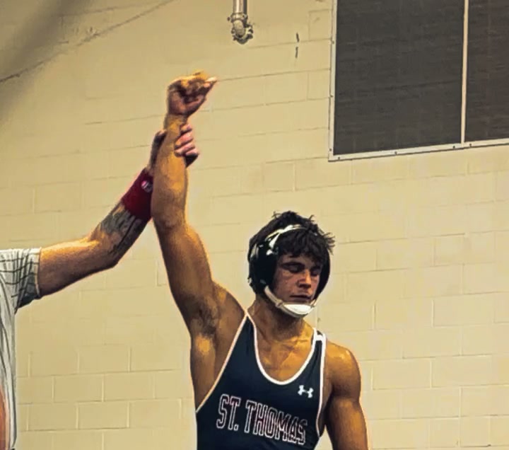 Diogo with his arm raised by the referee after a wrestling match, wearing a St. Thomas singlet
